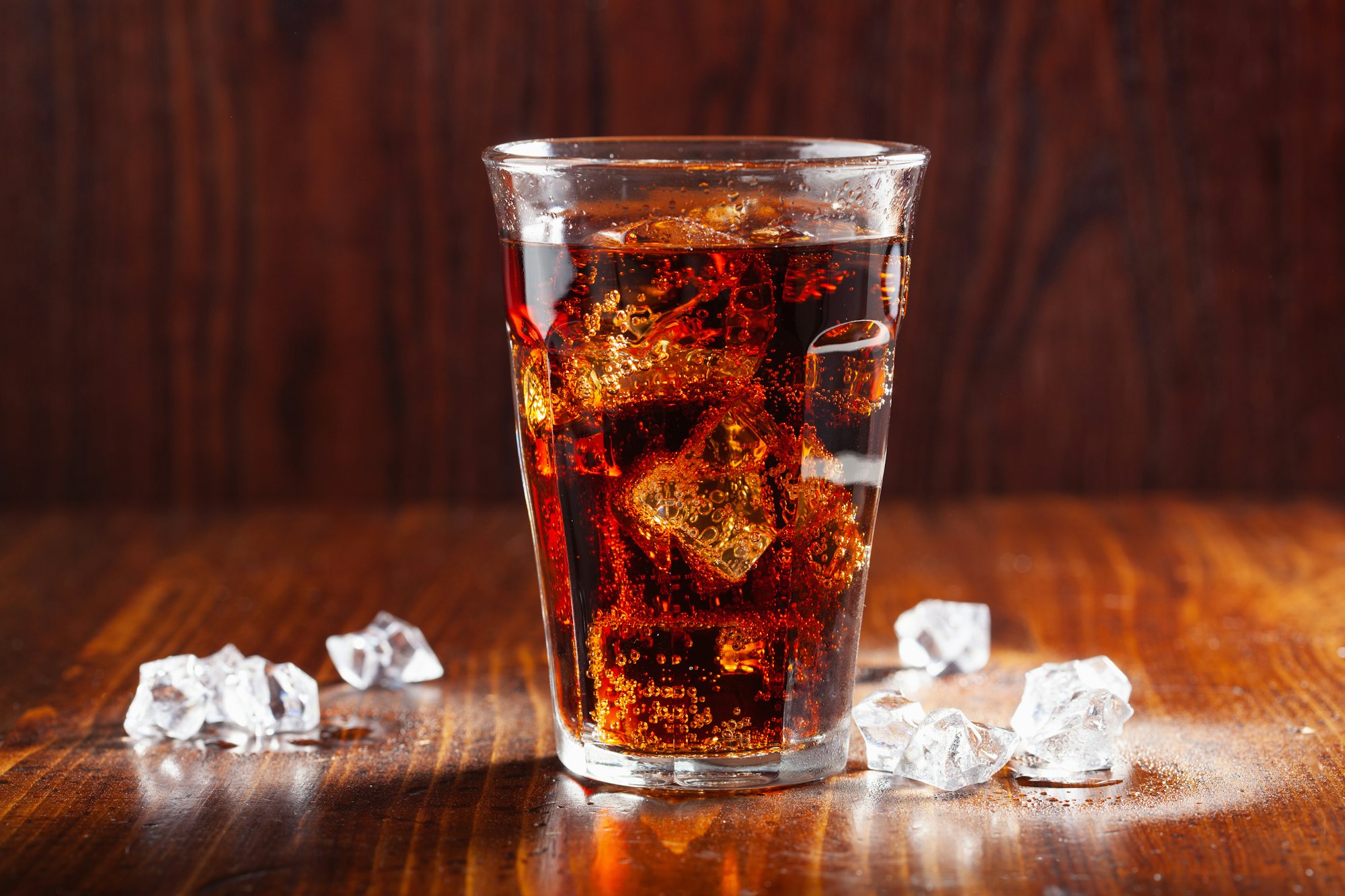 glass of cold cola soft drink with ice on wooden background